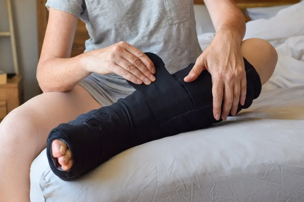 Woman sitting on bed putting on night compression wrap on lymphedema affected leg

