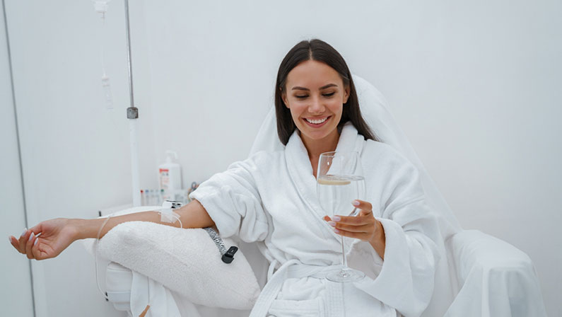 Beautiful woman in white bathrobe drink water during medical procedure in beauty clinic