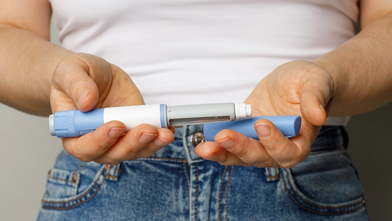 Diabetes blue Insulin or Semaglutide Injection pen closeup. Semaglutide or insulin drug against female belly. Semaglutide, Diabetes and Weight Loss concept.