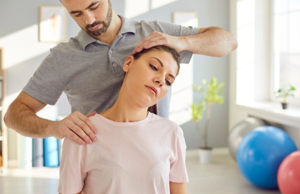 Masseur therapist specializing in physiotherapy and rehabilitation, providing a neck massage or stretching session for a patient in a medical office.