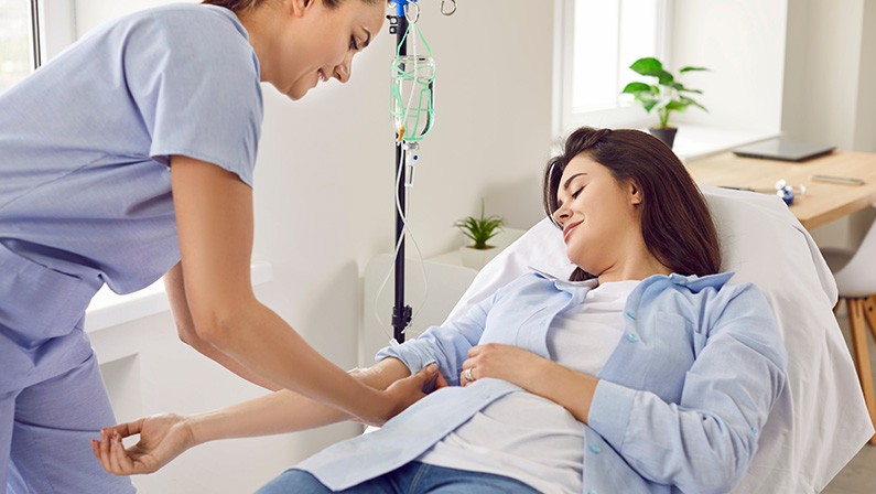 Female nurse doing IV drip therapy to a woman in medical clinic.